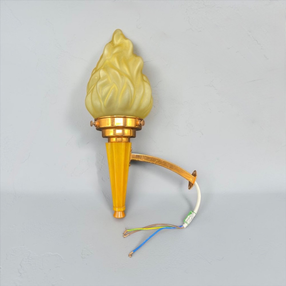 An Art Deco torch wall sconce featuring an amber flame-shaped moulded glass shade set on a yellow stepped stem with a brass mounting arm.