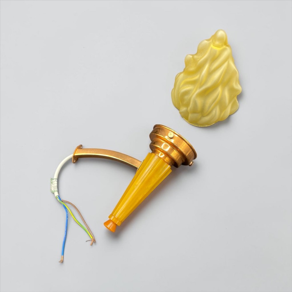 An Art Deco torch wall sconce featuring an amber flame-shaped moulded glass shade set on a yellow stepped stem with a brass mounting arm. View V