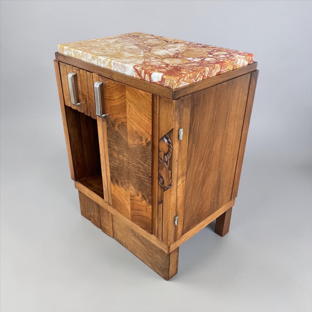 An Art Deco bedside cabinet crafted from polished brown walnut wood featuring a variegated reddish marble top surface and metal handles.