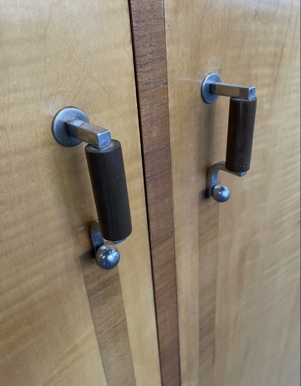 An Art Deco stepped blonde wood cabinet featuring a full-length door on the right, a smaller lower cabinet and top drawer on the left, fitted with vertical bar handles. View VII