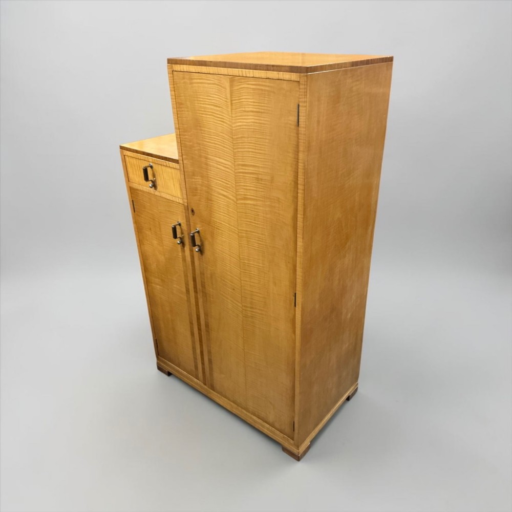 An Art Deco stepped blonde wood cabinet featuring a full-length door on the right, a smaller lower cabinet and top drawer on the left, fitted with vertical bar handles. View VIII