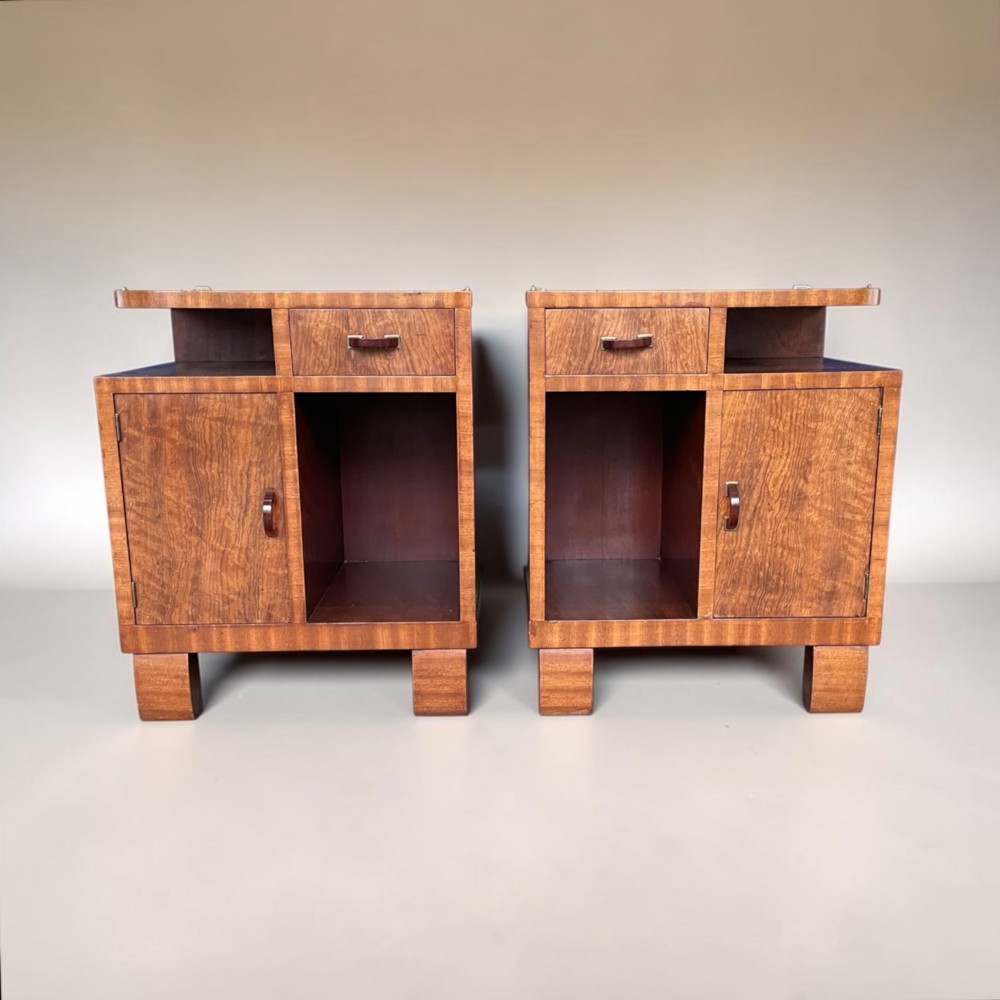 A pair of matching warm brown wooden Art Deco bedside cabinets with asymmetrical drawers, open shelves, lower cupboards, and block feet.