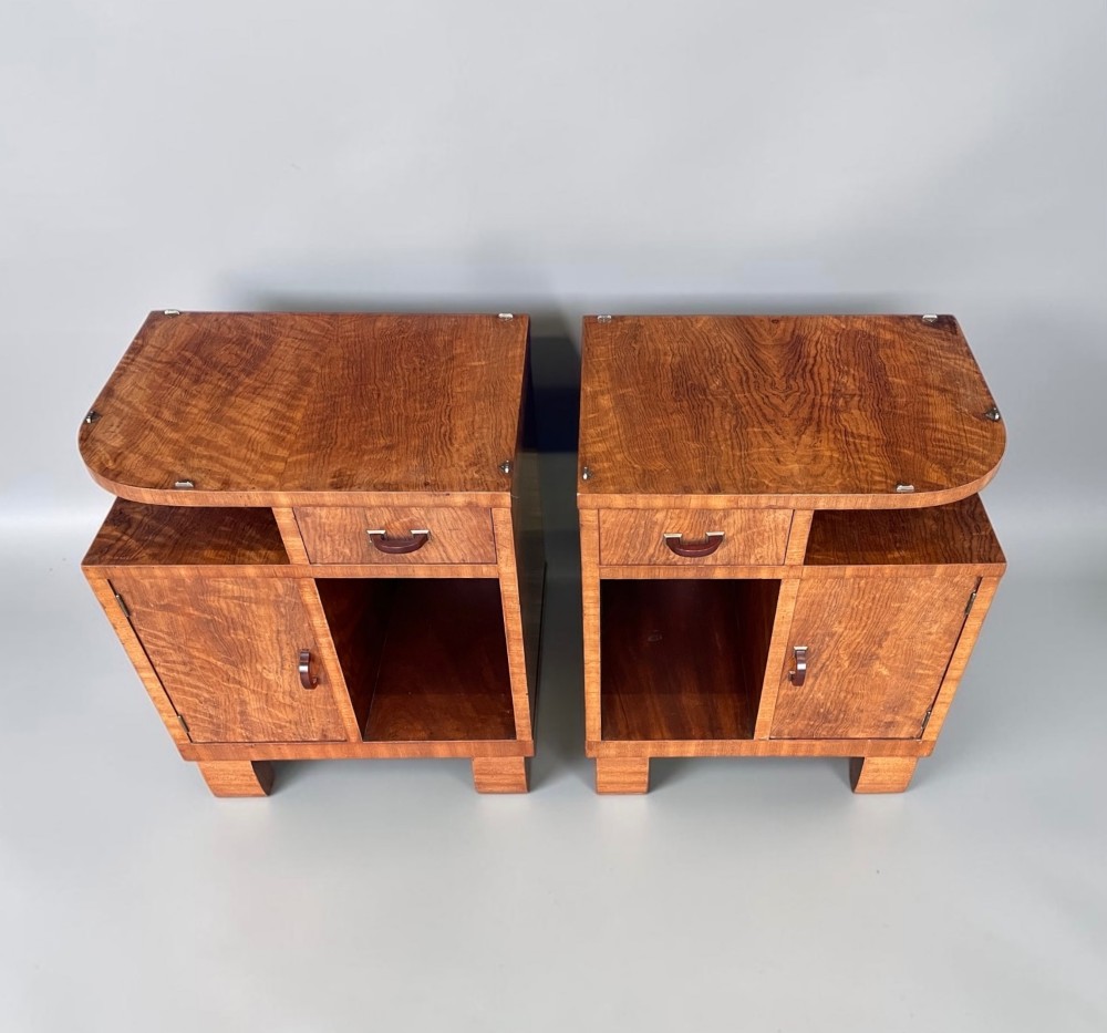 A pair of matching warm brown wooden Art Deco bedside cabinets with asymmetrical drawers, open shelves, lower cupboards, and block feet. View X
