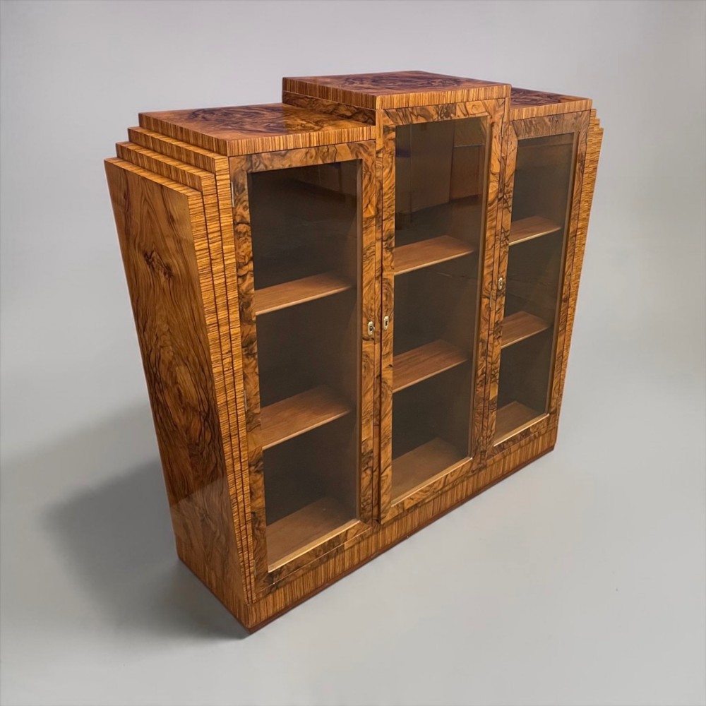 An Art Deco warm brown walnut bookcase featuring a stepped architectural top, three glass doors, and highly figured timber veneer. View II