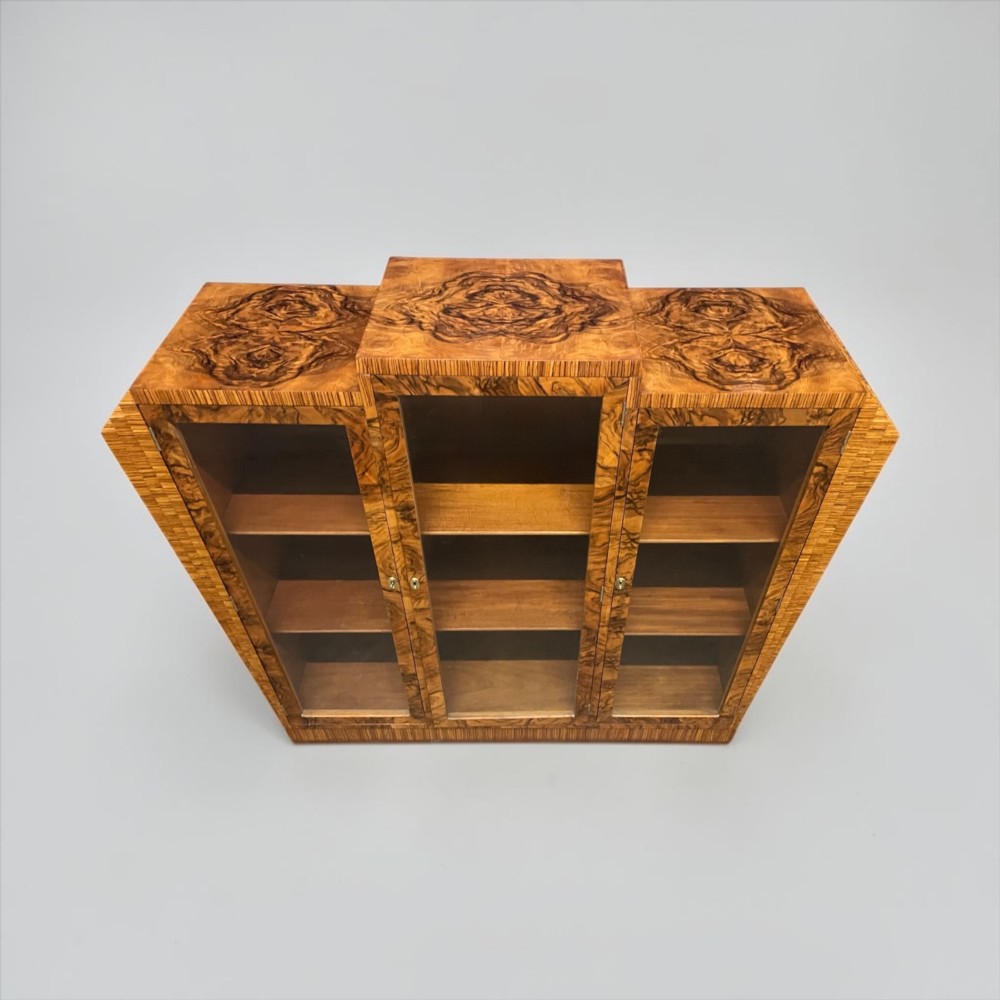An Art Deco warm brown walnut bookcase featuring a stepped architectural top, three glass doors, and highly figured timber veneer. View IV