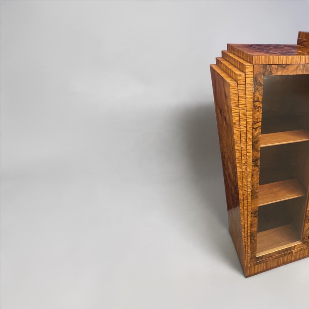 An Art Deco warm brown walnut bookcase featuring a stepped architectural top, three glass doors, and highly figured timber veneer. View VIII
