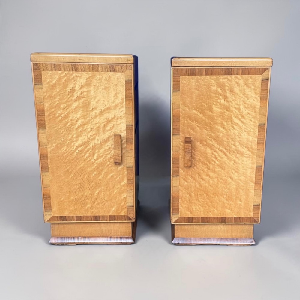 A matching pair of golden burr maple Art Deco bedside tables featuring single door cupboards with wooden block handles and plinth bases.