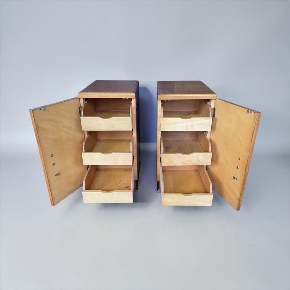 A matching pair of golden burr maple Art Deco bedside tables featuring single door cupboards with wooden block handles and plinth bases. View V