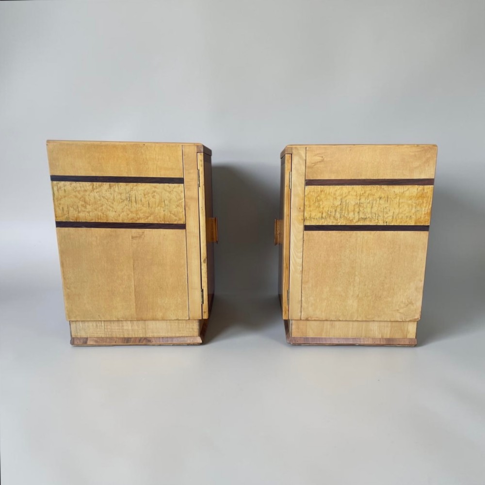 A matching pair of golden burr maple Art Deco bedside tables featuring single door cupboards with wooden block handles and plinth bases. View VI