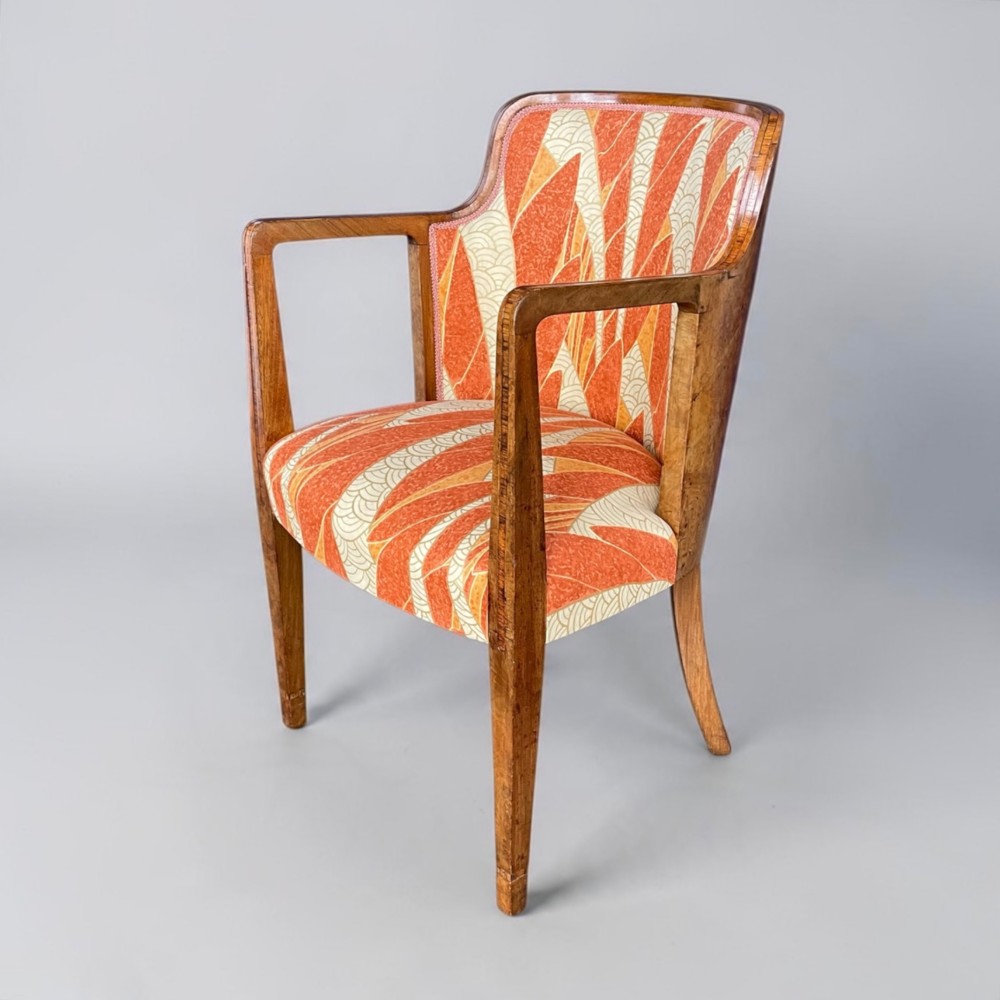 An Art Deco armchair featuring a polished walnut wooden frame, geometric orange patterned upholstery, angular armrests, and tapered legs.