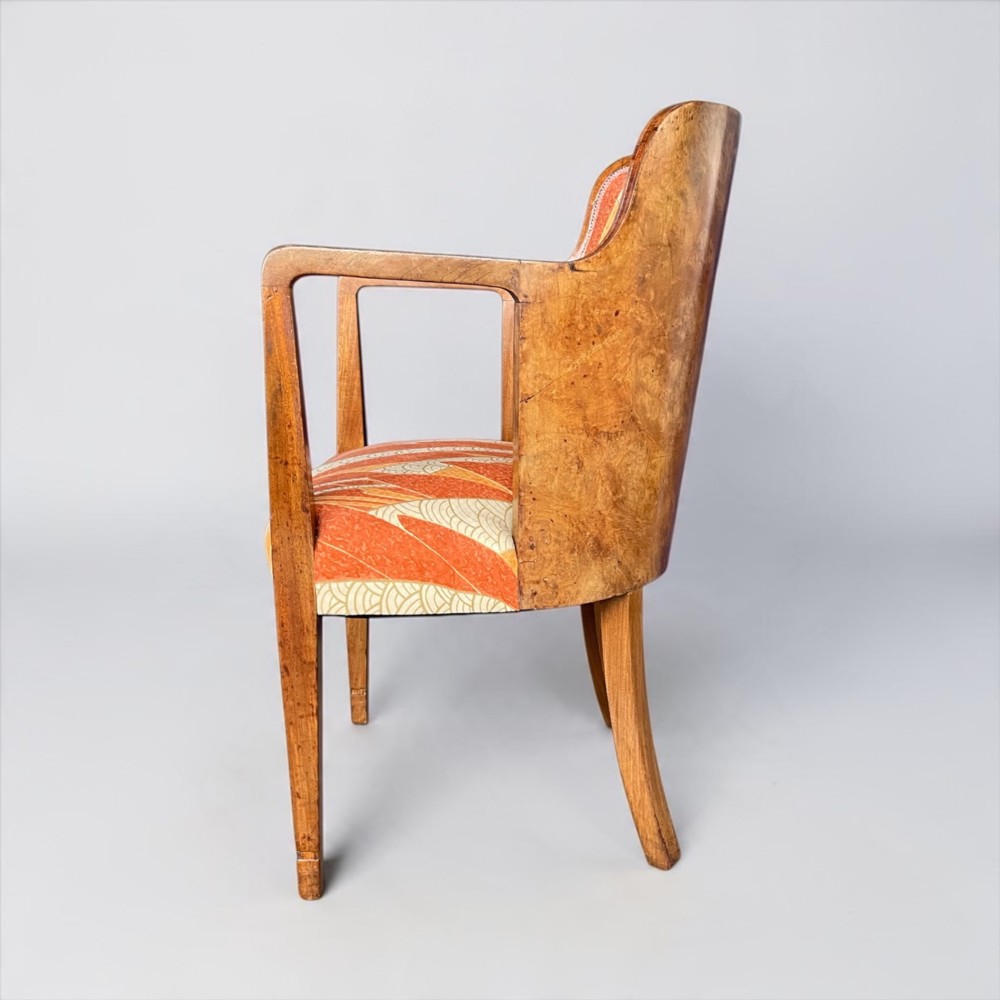 An Art Deco armchair featuring a polished walnut wooden frame, geometric orange patterned upholstery, angular armrests, and tapered legs. View II