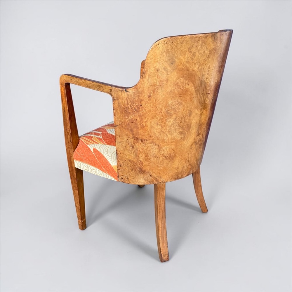 An Art Deco armchair featuring a polished walnut wooden frame, geometric orange patterned upholstery, angular armrests, and tapered legs. View III