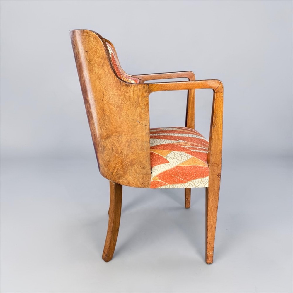 An Art Deco armchair featuring a polished walnut wooden frame, geometric orange patterned upholstery, angular armrests, and tapered legs. View VI