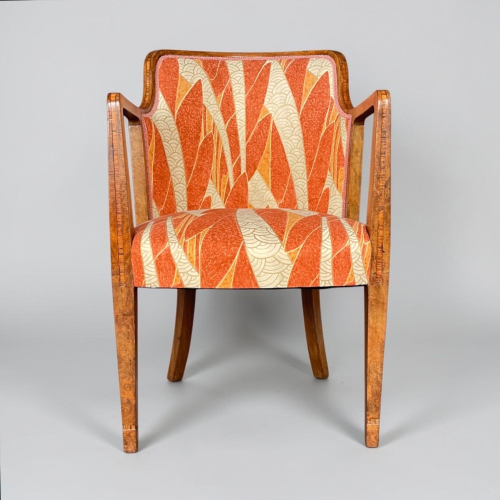 An Art Deco armchair featuring a polished walnut wooden frame, geometric orange patterned upholstery, angular armrests, and tapered legs. View VII