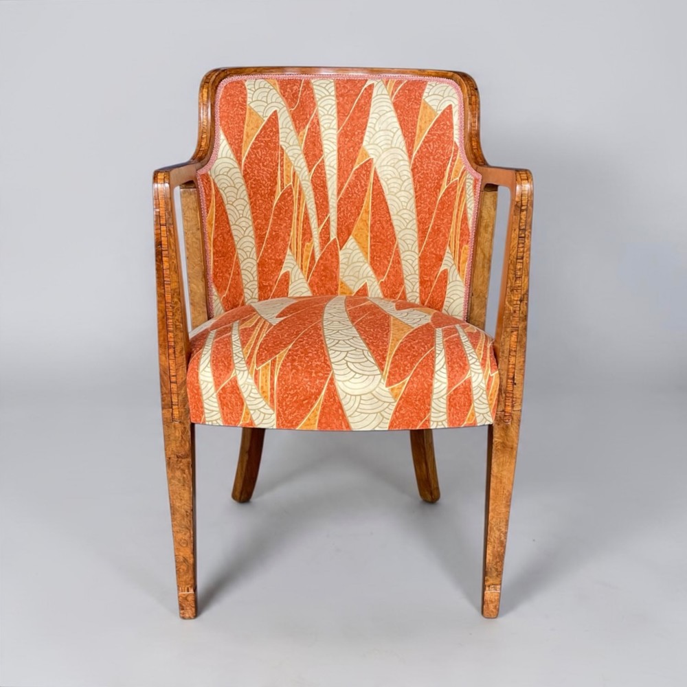 An Art Deco armchair featuring a polished walnut wooden frame, geometric orange patterned upholstery, angular armrests, and tapered legs. View VIII