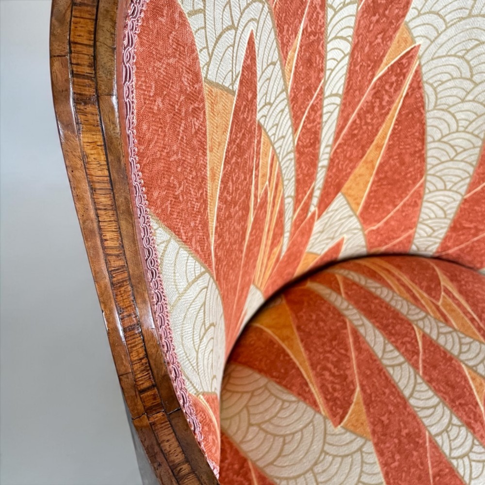 An Art Deco armchair featuring a polished walnut wooden frame, geometric orange patterned upholstery, angular armrests, and tapered legs. View XI