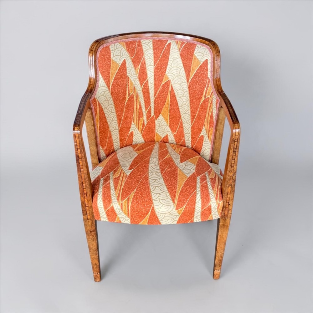 An Art Deco armchair featuring a polished walnut wooden frame, geometric orange patterned upholstery, angular armrests, and tapered legs. View XII