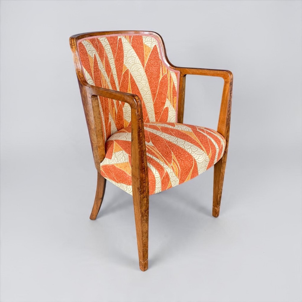 An Art Deco armchair featuring a polished walnut wooden frame, geometric orange patterned upholstery, angular armrests, and tapered legs. View XIII