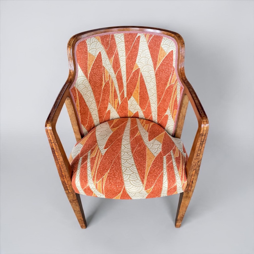 An Art Deco armchair featuring a polished walnut wooden frame, geometric orange patterned upholstery, angular armrests, and tapered legs. View XIV