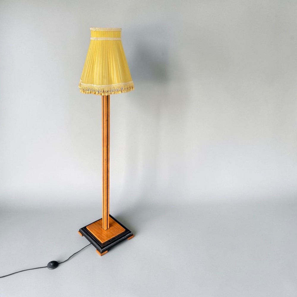 An Art Deco standard lamp featuring a straight wooden column, a stepped square base with ebonised trim, and a yellow pleated fabric shade with fringe detailing. View II