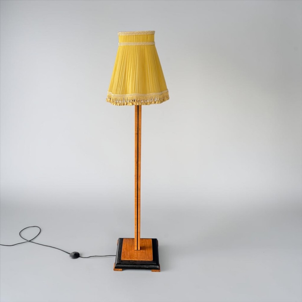 An Art Deco standard lamp featuring a straight wooden column, a stepped square base with ebonised trim, and a yellow pleated fabric shade with fringe detailing. View III