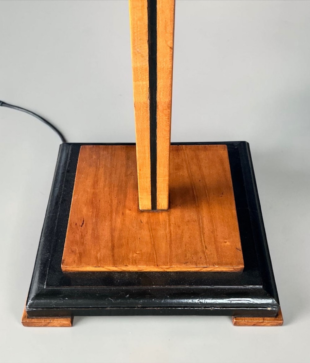 An Art Deco standard lamp featuring a straight wooden column, a stepped square base with ebonised trim, and a yellow pleated fabric shade with fringe detailing. View IV