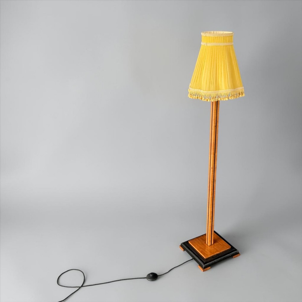 An Art Deco standard lamp featuring a straight wooden column, a stepped square base with ebonised trim, and a yellow pleated fabric shade with fringe detailing. View V