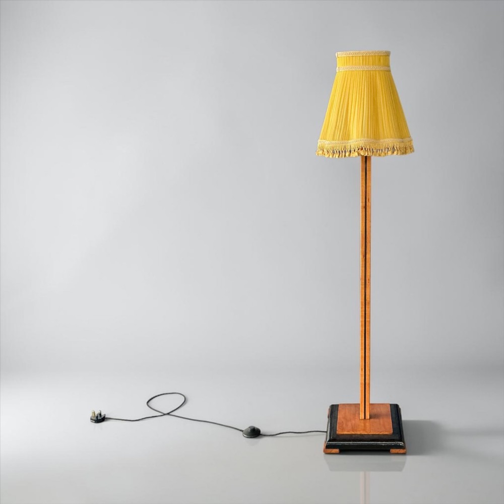 An Art Deco standard lamp featuring a straight wooden column, a stepped square base with ebonised trim, and a yellow pleated fabric shade with fringe detailing. View VI