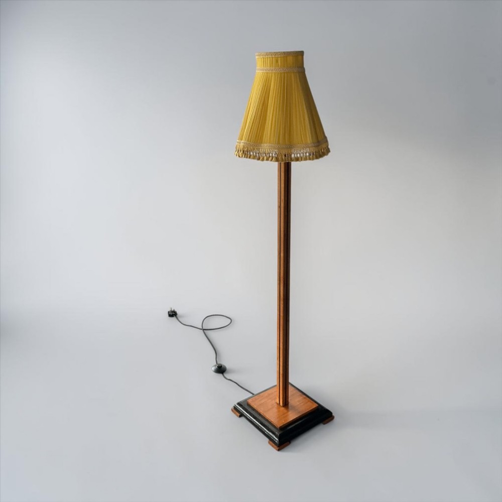 An Art Deco standard lamp featuring a straight wooden column, a stepped square base with ebonised trim, and a yellow pleated fabric shade with fringe detailing. View VII