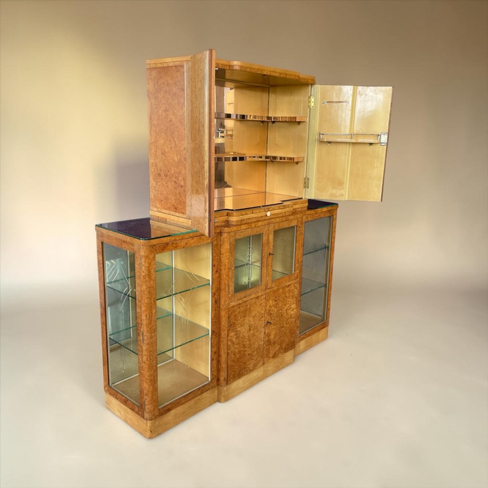 An Art Deco burr walnut cocktail cabinet with open upper doors revealing a mirrored interior, flanked by lower etched glass display sections.