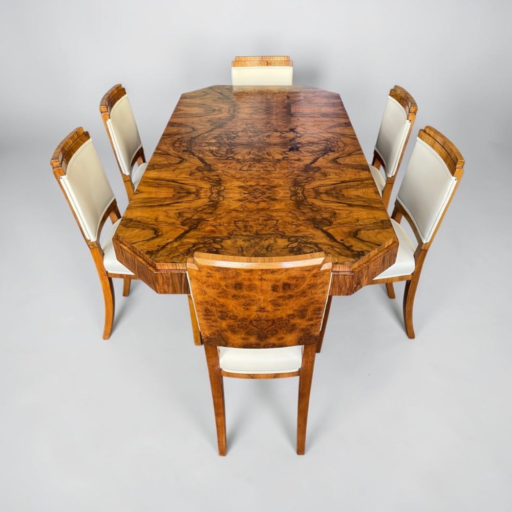 An Art Deco burr walnut dining table featuring a richly figured canted top paired with six matching chairs upholstered in cream leather. View IV