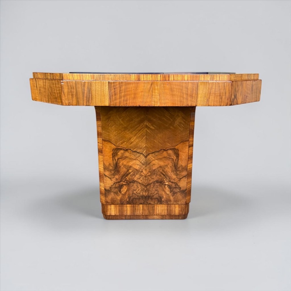 An Art Deco burr walnut dining table featuring a richly figured canted top paired with six matching chairs upholstered in cream leather. View V