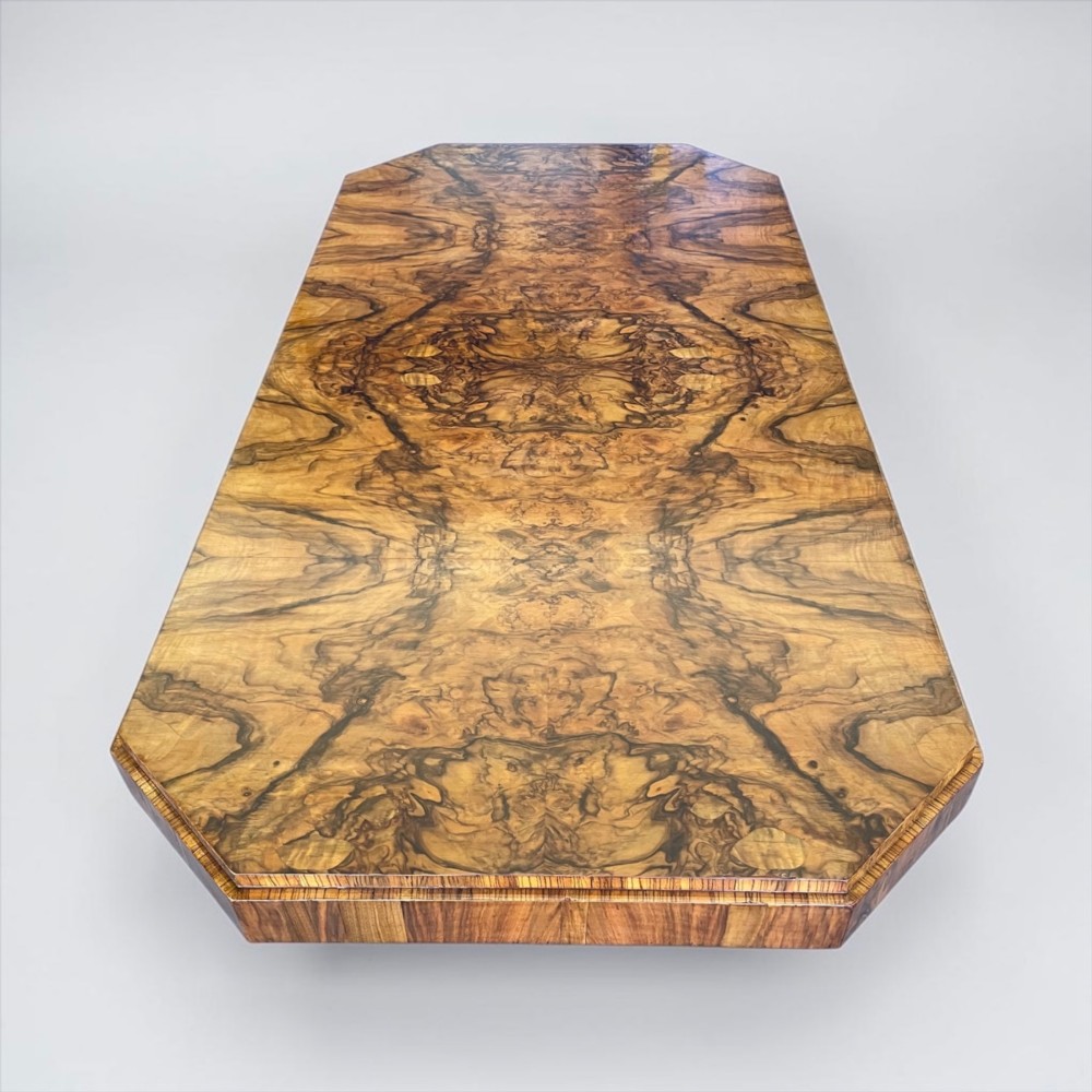 An Art Deco burr walnut dining table featuring a richly figured canted top paired with six matching chairs upholstered in cream leather. View VI