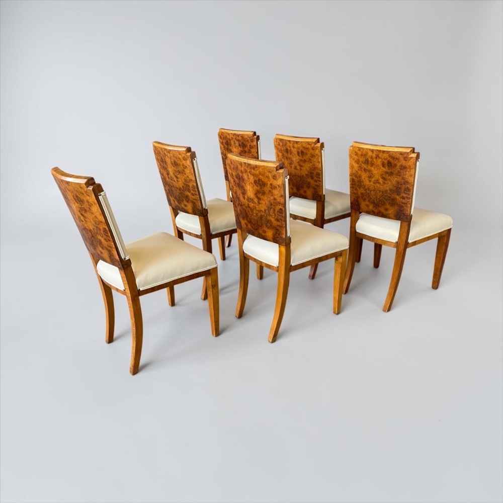 An Art Deco burr walnut dining table featuring a richly figured canted top paired with six matching chairs upholstered in cream leather. View VII
