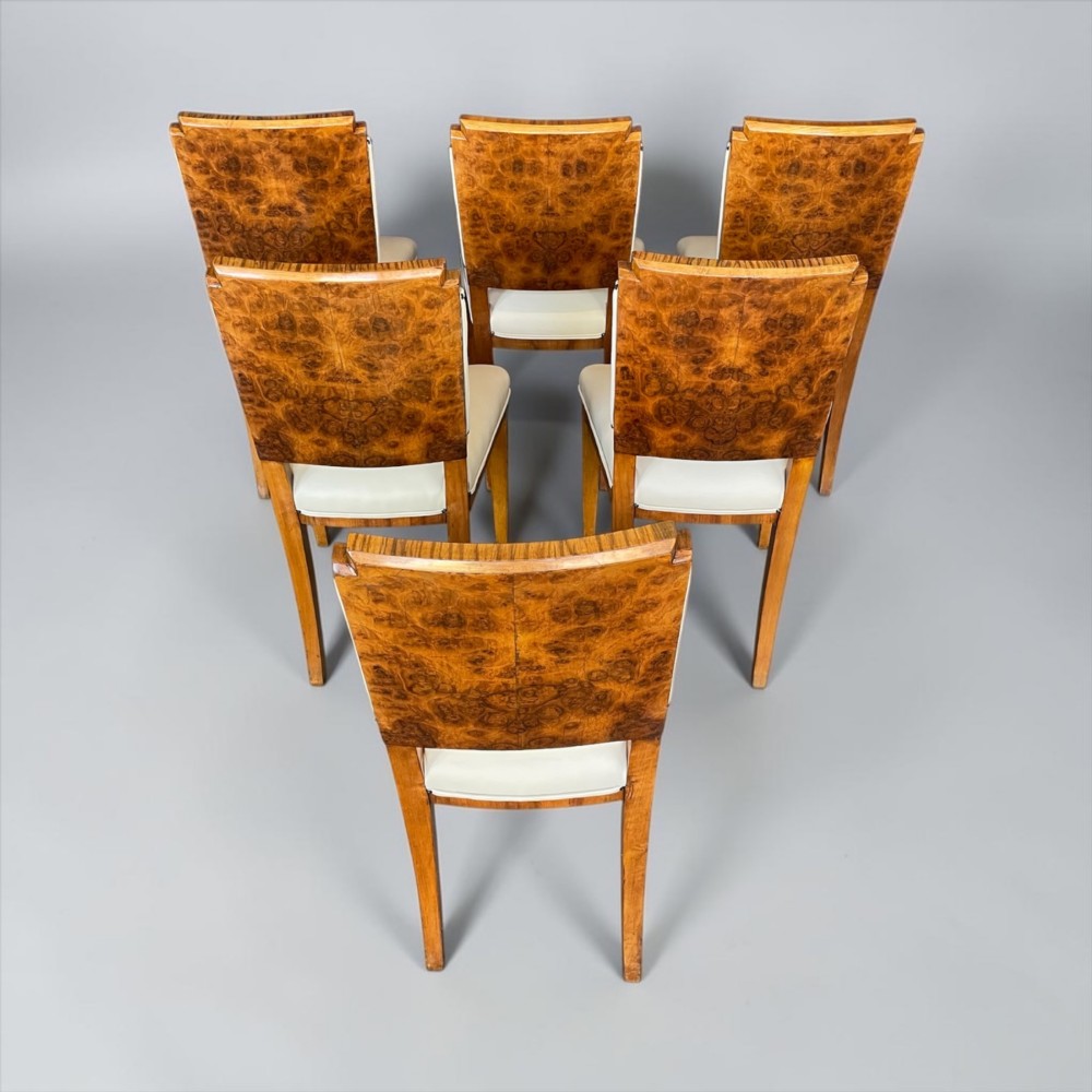 An Art Deco burr walnut dining table featuring a richly figured canted top paired with six matching chairs upholstered in cream leather. View VIII