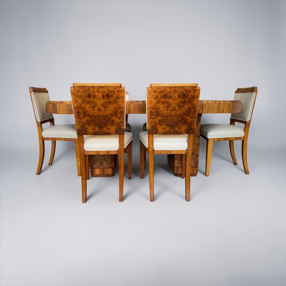 An Art Deco burr walnut dining table featuring a richly figured canted top paired with six matching chairs upholstered in cream leather. View XI