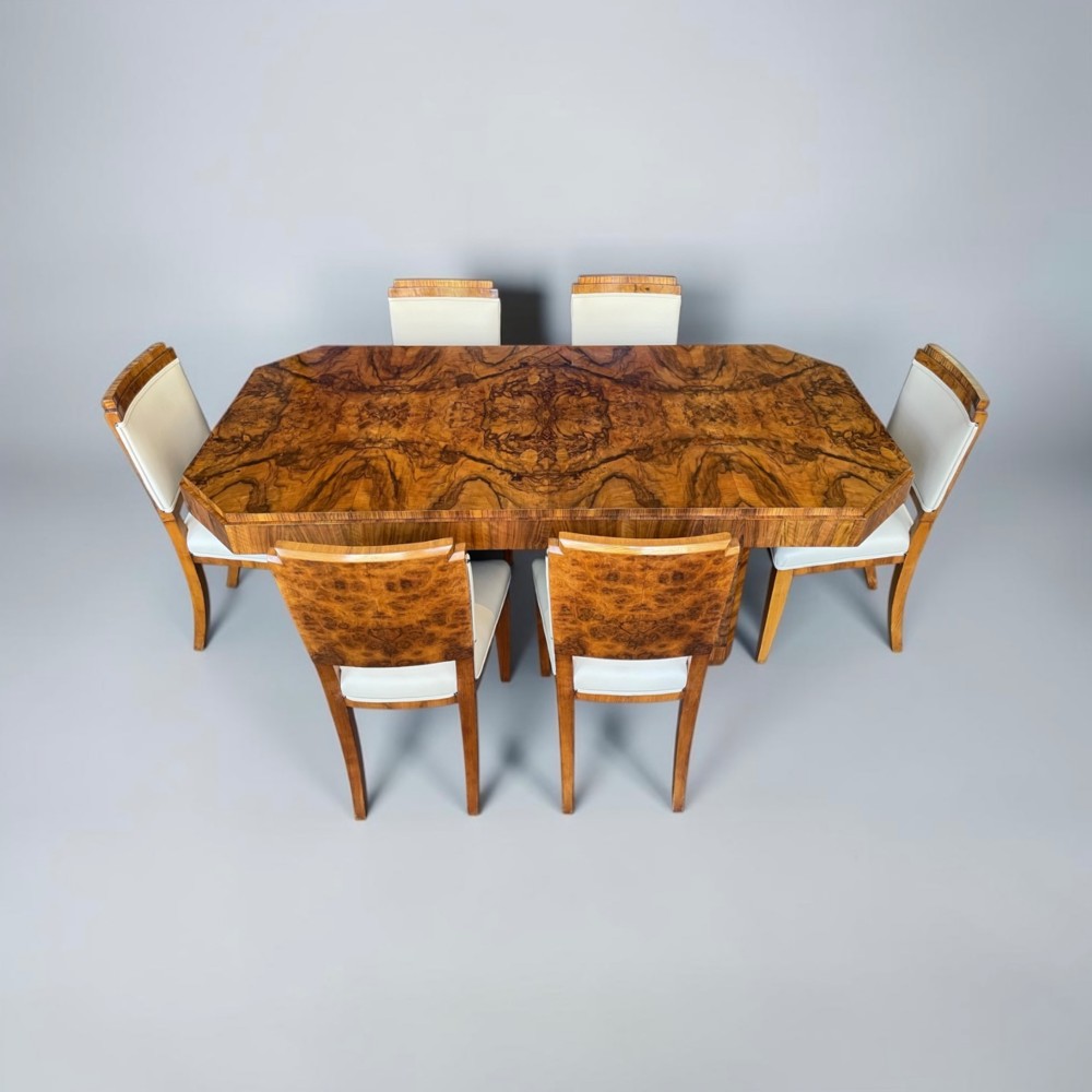 An Art Deco burr walnut dining table featuring a richly figured canted top paired with six matching chairs upholstered in cream leather. View XII