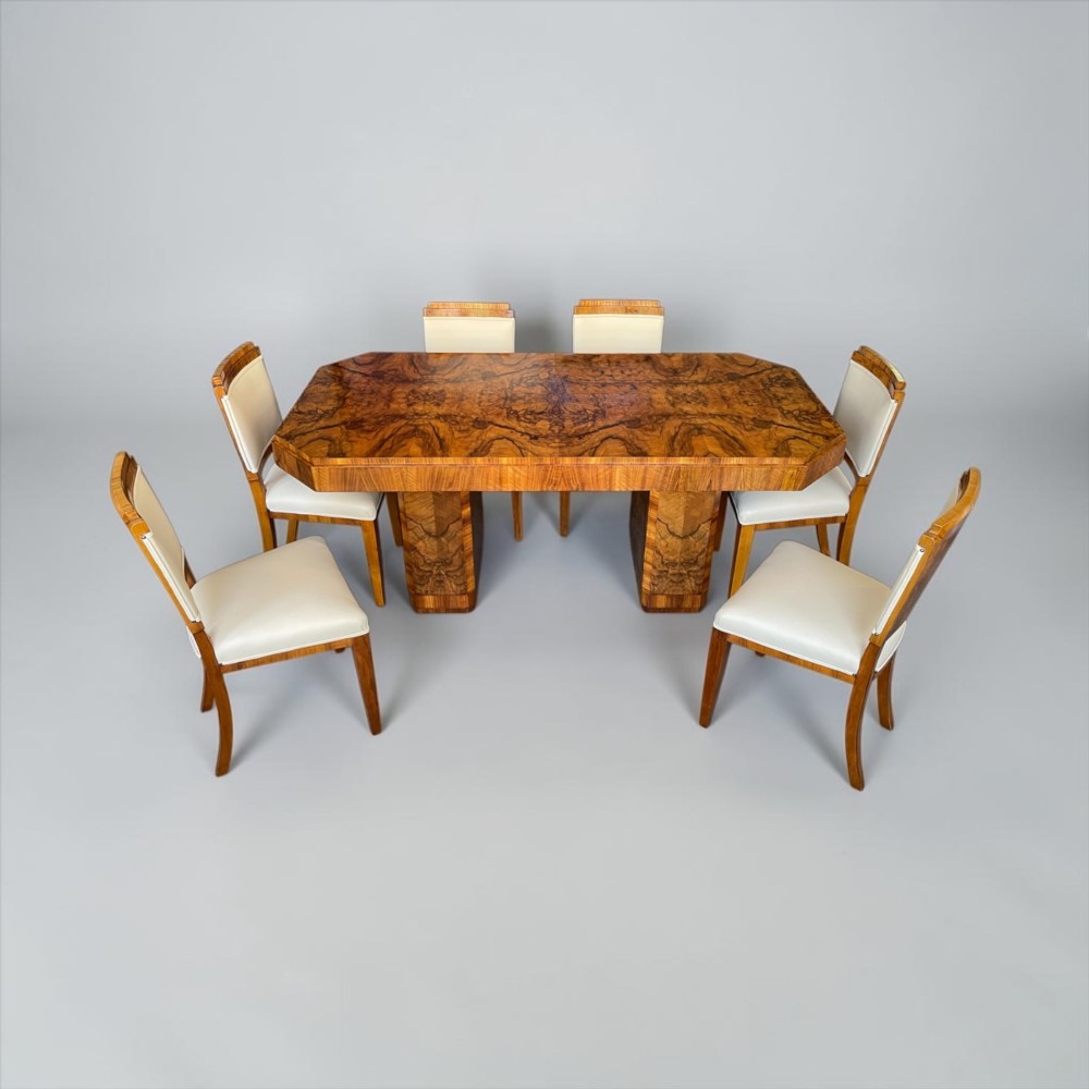 An Art Deco burr walnut dining table featuring a richly figured canted top paired with six matching chairs upholstered in cream leather. View XIII