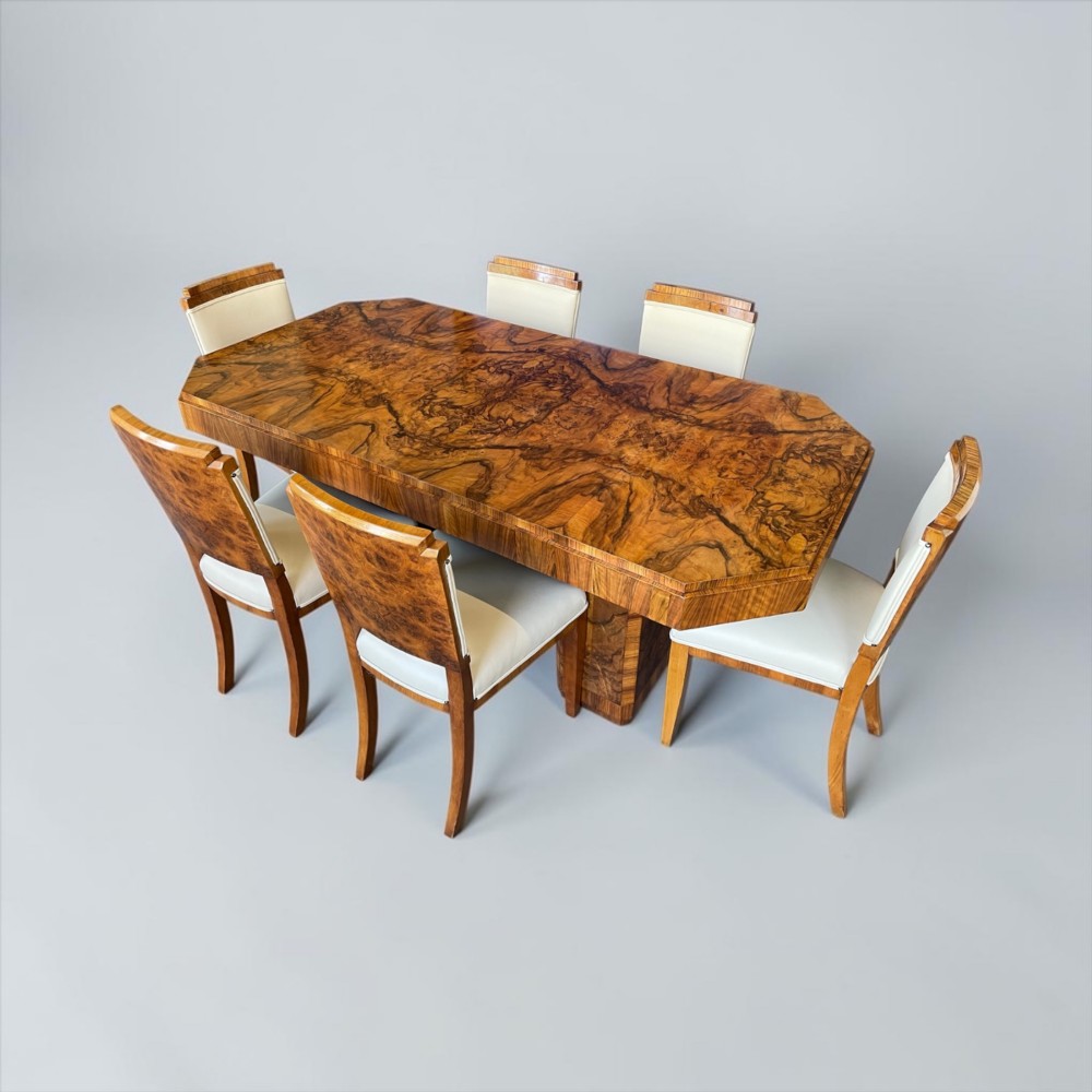 An Art Deco burr walnut dining table featuring a richly figured canted top paired with six matching chairs upholstered in cream leather. View XIV