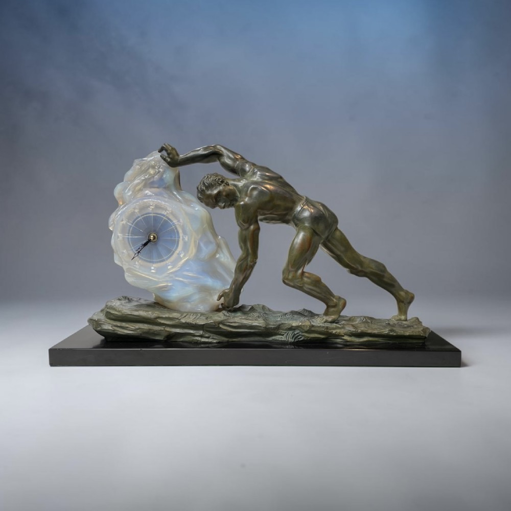 An Art Deco bronze sculpture featuring a athletic male figure pushing an opalescent glass rock containing an integrated clock face on a black base.