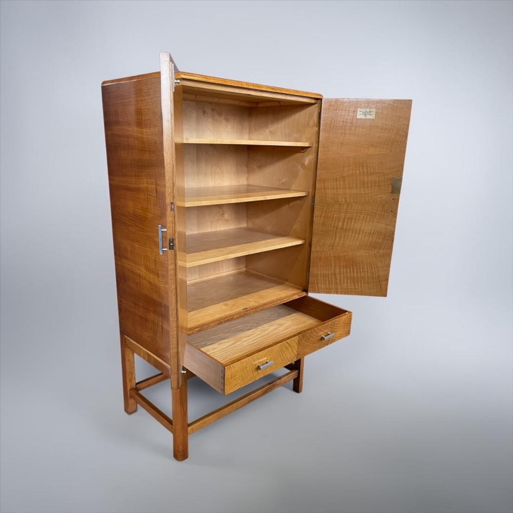 An Art Deco golden oak cabinet on stand featuring book-matched chevron wood veneers, two lower drawers, twin cupboard doors, and metal handles. View II