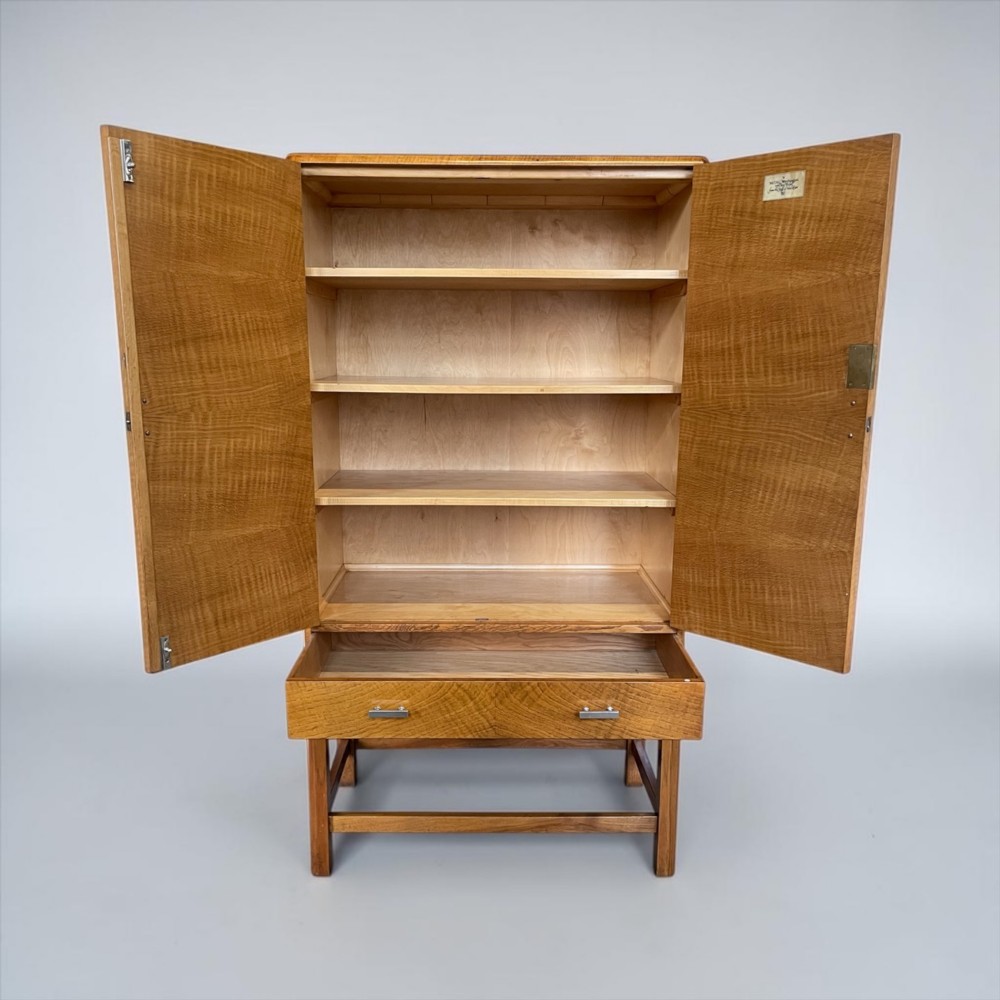 An Art Deco golden oak cabinet on stand featuring book-matched chevron wood veneers, two lower drawers, twin cupboard doors, and metal handles. View V