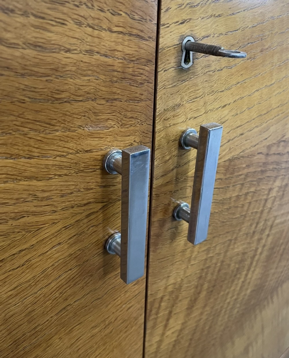 An Art Deco golden oak cabinet on stand featuring book-matched chevron wood veneers, two lower drawers, twin cupboard doors, and metal handles. View VI