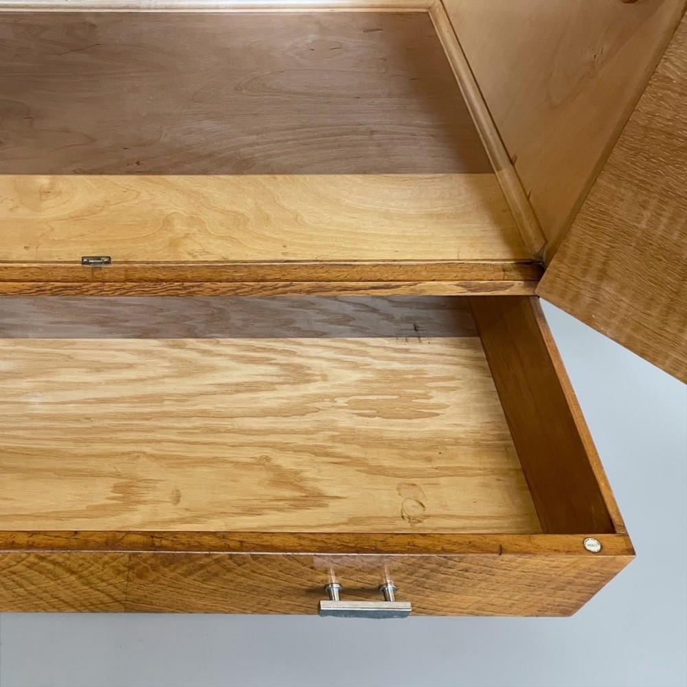 An Art Deco golden oak cabinet on stand featuring book-matched chevron wood veneers, two lower drawers, twin cupboard doors, and metal handles. View VII