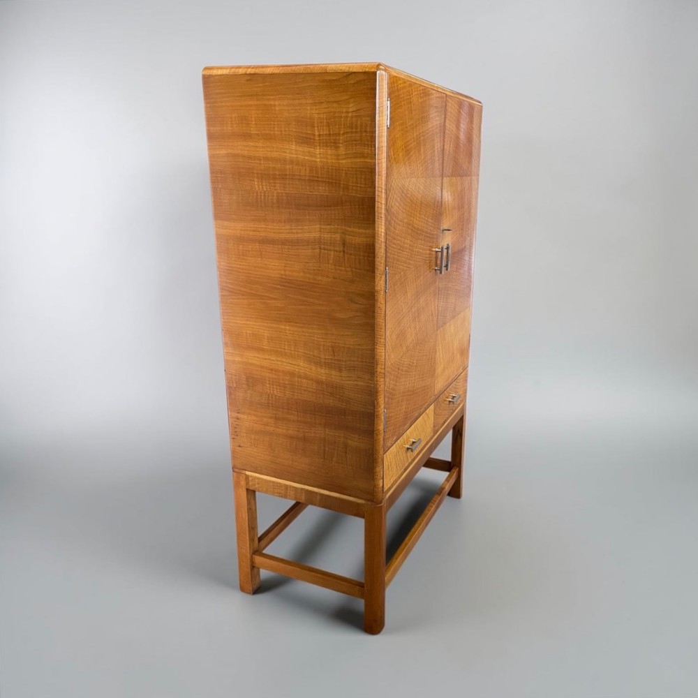 An Art Deco golden oak cabinet on stand featuring book-matched chevron wood veneers, two lower drawers, twin cupboard doors, and metal handles. View XV