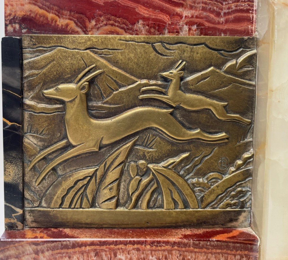 An Art Deco stepped mantel clock crafted from cream onyx and red marble with relief bronze panels depicting gazelles and a panther. View II