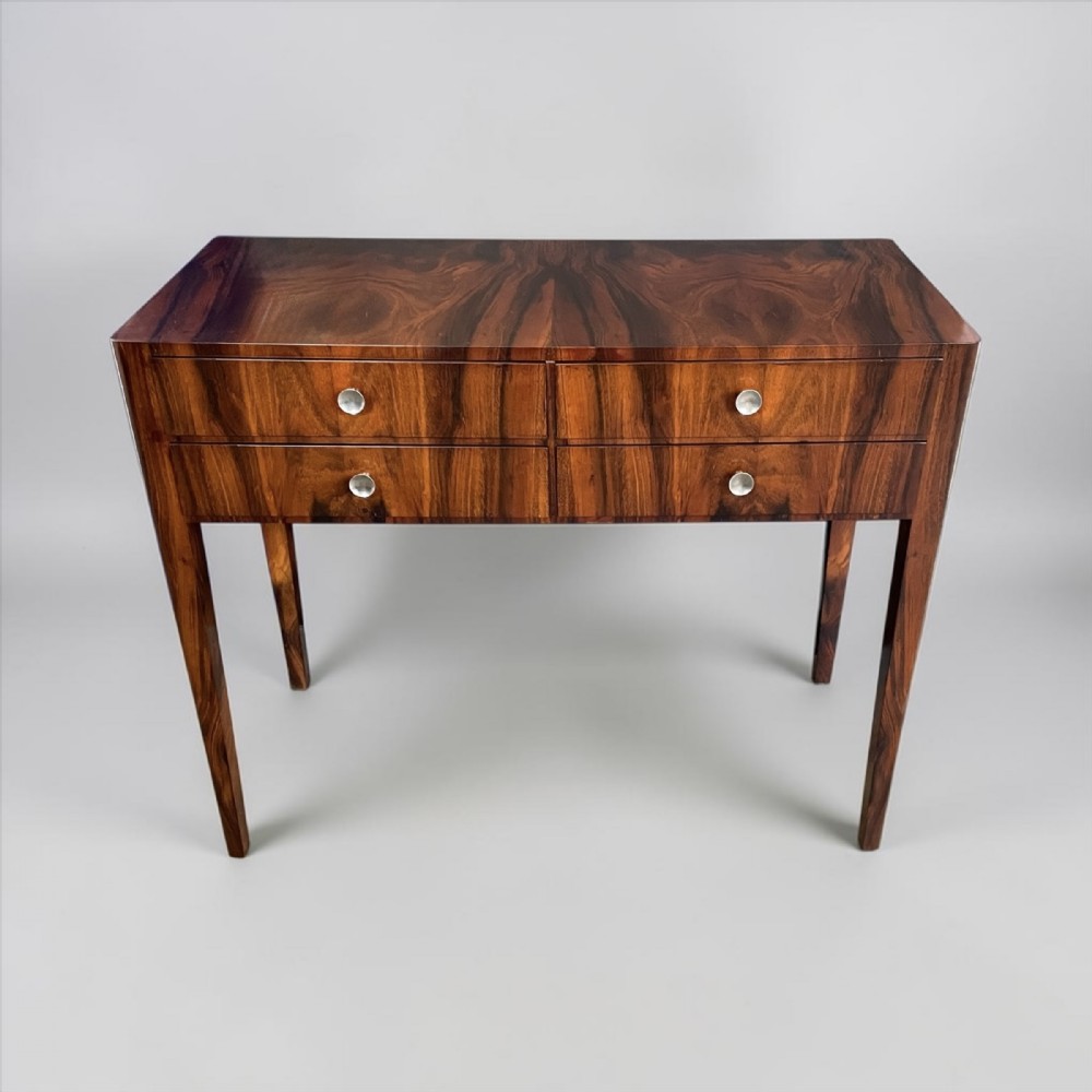 An Art Deco rosewood side table featuring rich bookmatched wood grain, four drawers with circular silver-toned knobs, and four tapered legs.