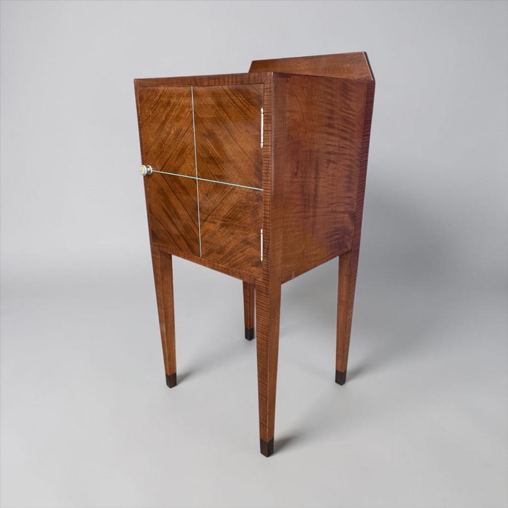 An Art Deco figured walnut bedside table featuring a raised gallery back, geometric parquetry double doors, and slender tapered legs. View II