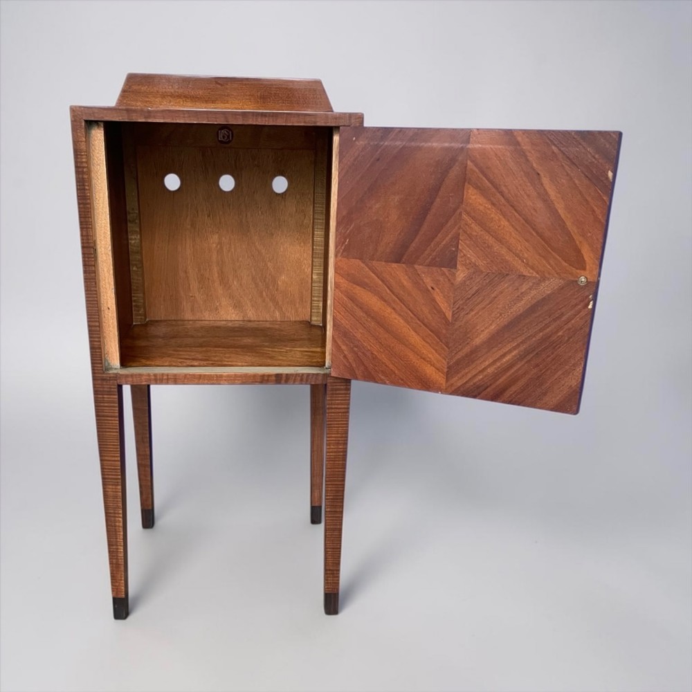 An Art Deco figured walnut bedside table featuring a raised gallery back, geometric parquetry double doors, and slender tapered legs. View III