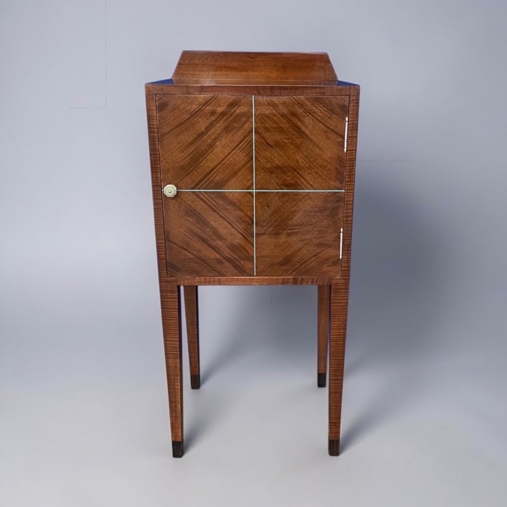 An Art Deco figured walnut bedside table featuring a raised gallery back, geometric parquetry double doors, and slender tapered legs. View IV